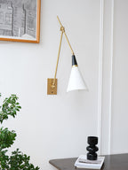 Clérachic wall light on a white wall beside a framed print, with a white cone shade on a long brass arm and a small black vase below.