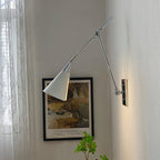 Clérachic wall light in bright nickel, with a white cone shade, beside a framed garden print and a sheer lace curtain.