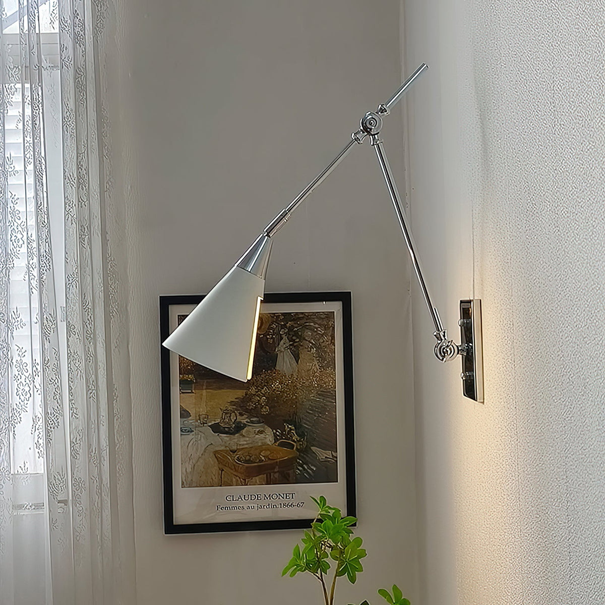 Clérachic wall light in bright nickel, with a white cone shade, beside a framed garden print and a sheer lace curtain.