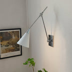 Clérachic wall light in bright nickel, with a white cone shade and a dark backplate, beside a framed garden print and a green plant.