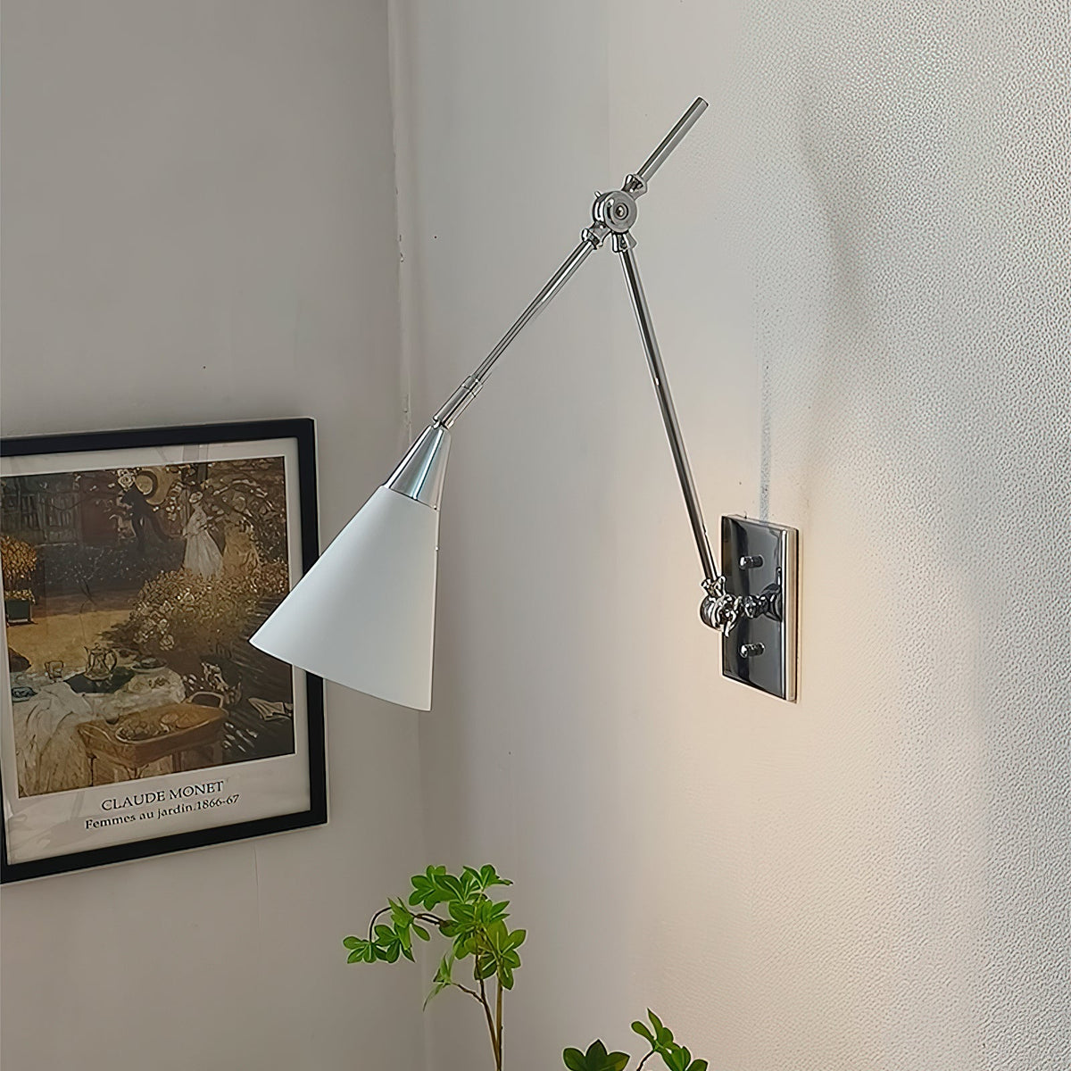 Clérachic wall light in bright nickel, with a white cone shade and a dark backplate, beside a framed garden print and a green plant.