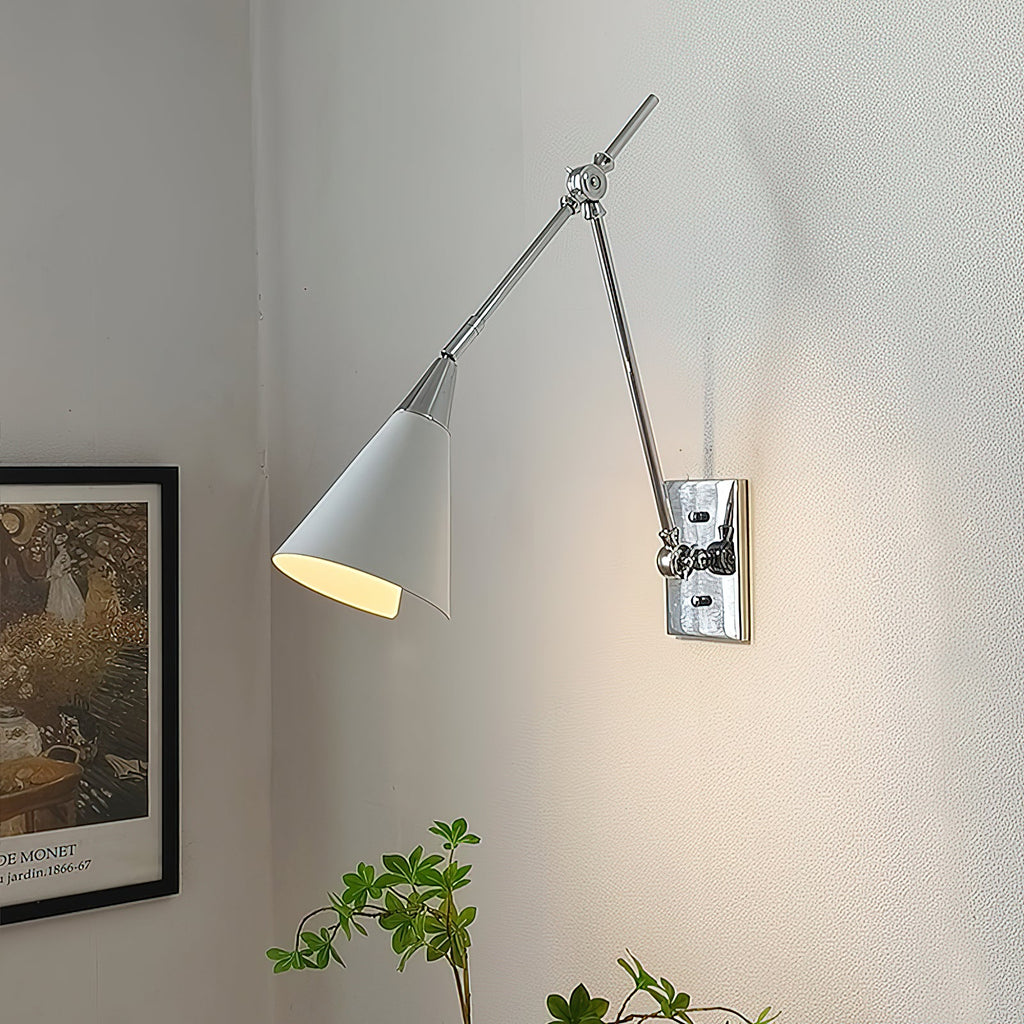 Clérachic wall light in bright nickel, with a white cone shade lit inside, beside a framed garden print on a pale wall.