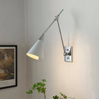 Clérachic wall light in bright nickel, with a white cone shade lit inside, beside a framed garden print on a pale wall.