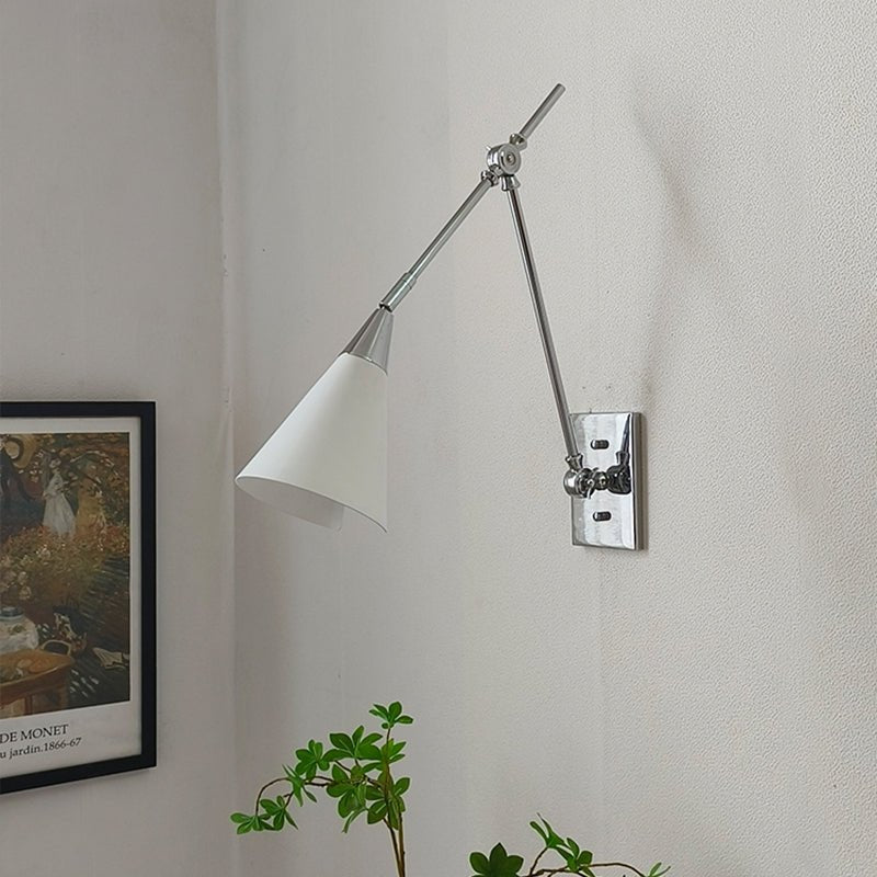 Clérachic wall light with a bright nickel arm and a white cone shade beside a framed print, with a plant at the bottom.