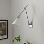 Clérachic wall light with a bright nickel arm and a white cone shade beside a framed print, with a plant at the bottom.