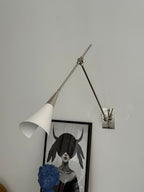 Clérachic wall light in nickel with a white cone shade tilted down, in front of a framed portrait and a blue sculpture.