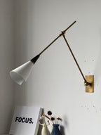 Clérachic wall light with a white cone shade and a black neck on a long brass arm, above a white framed print and a small blue vase.
