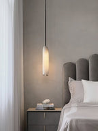 The Clérachic Asbury hangs beside a bed with a scalloped grey velvet headboard, dropping low over a dark nightstand.