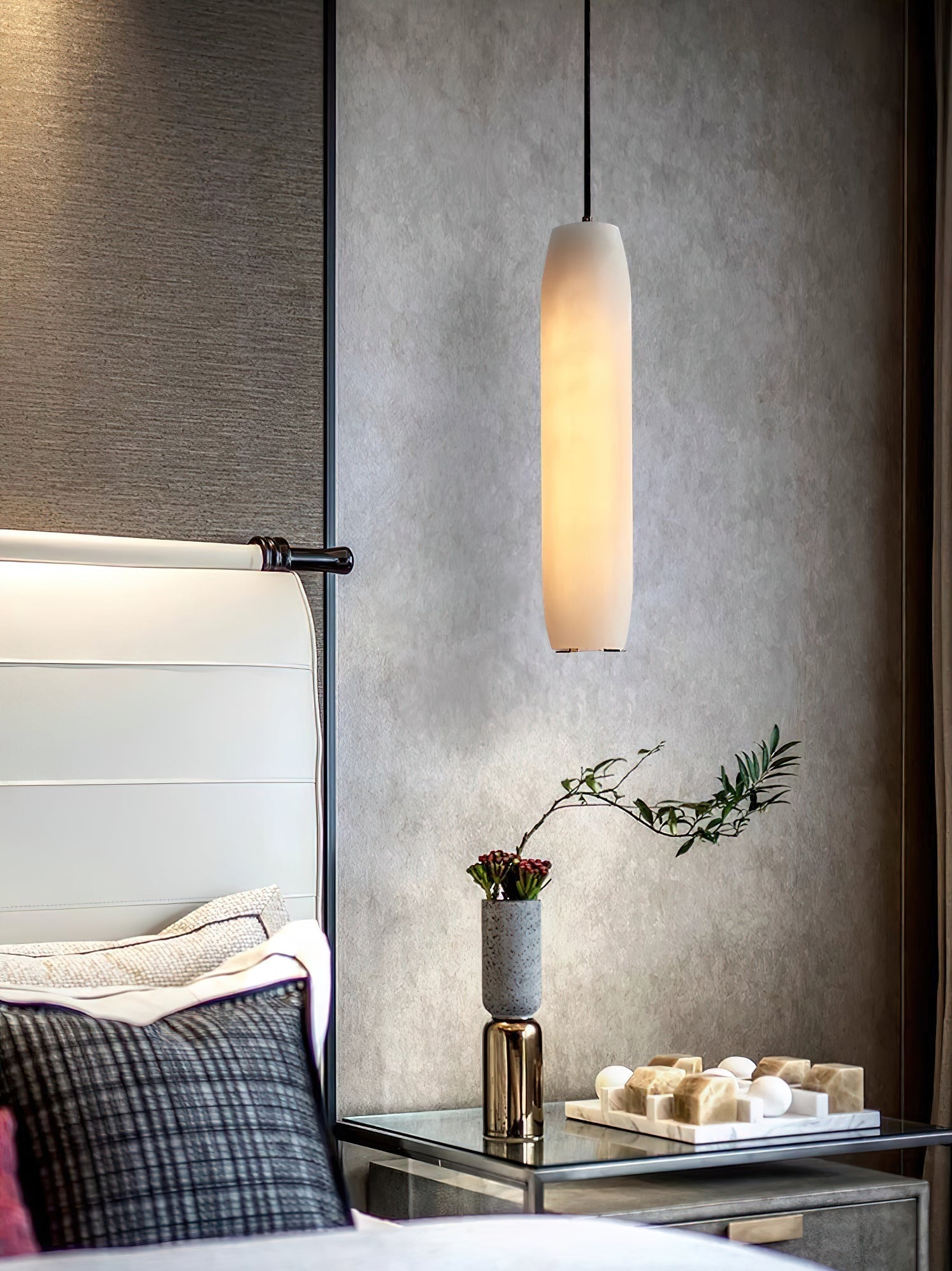 The Clérachic Asbury drops against a grey plaster wall above a glass bedside table set with a small vase and tray.