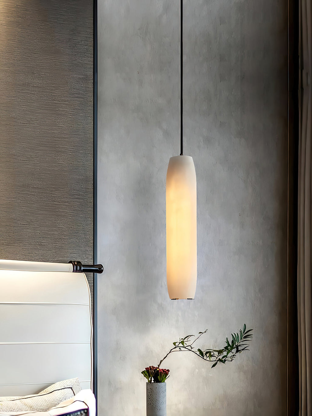 The Clérachic Asbury glows against grey plaster, an olive sprig in a stone pot below and a white headboard alongside.