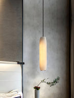 The Clérachic Asbury glows against grey plaster, an olive sprig in a stone pot below and a white headboard alongside.