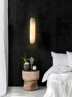 Clérachic sets the Asbury against a black textured wall, lighting a carved wood stump table beside crisp white bedding.