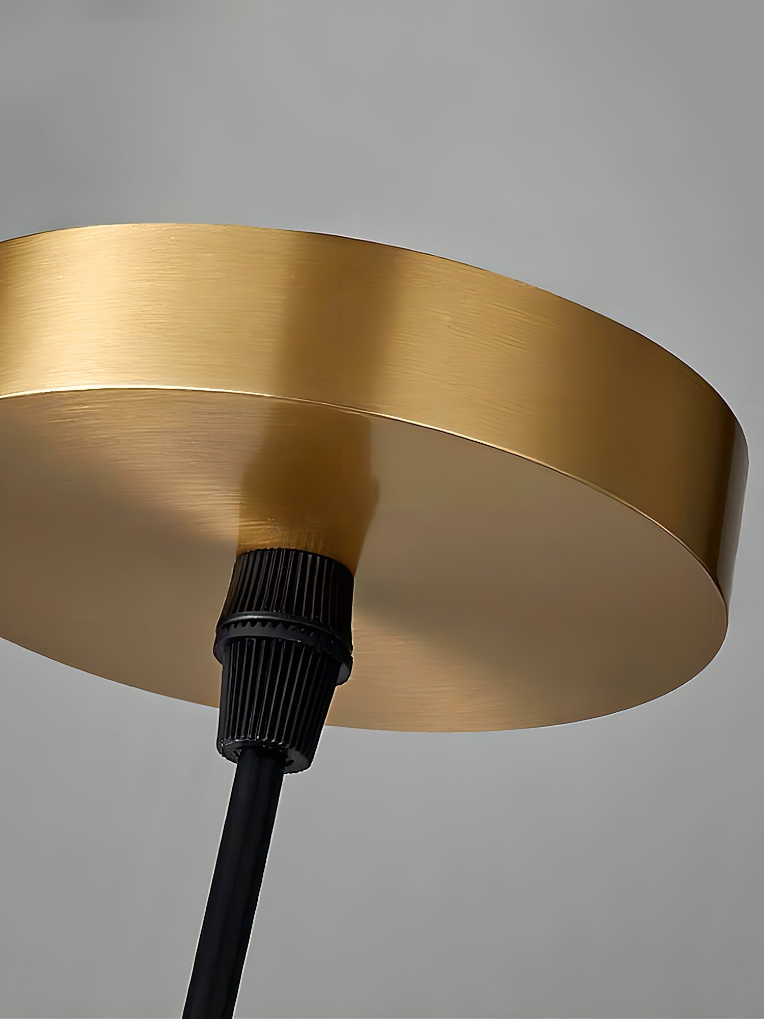 The Clérachic Asbury's brushed brass ceiling canopy seen close up, with the black cable grip fixed at its centre.