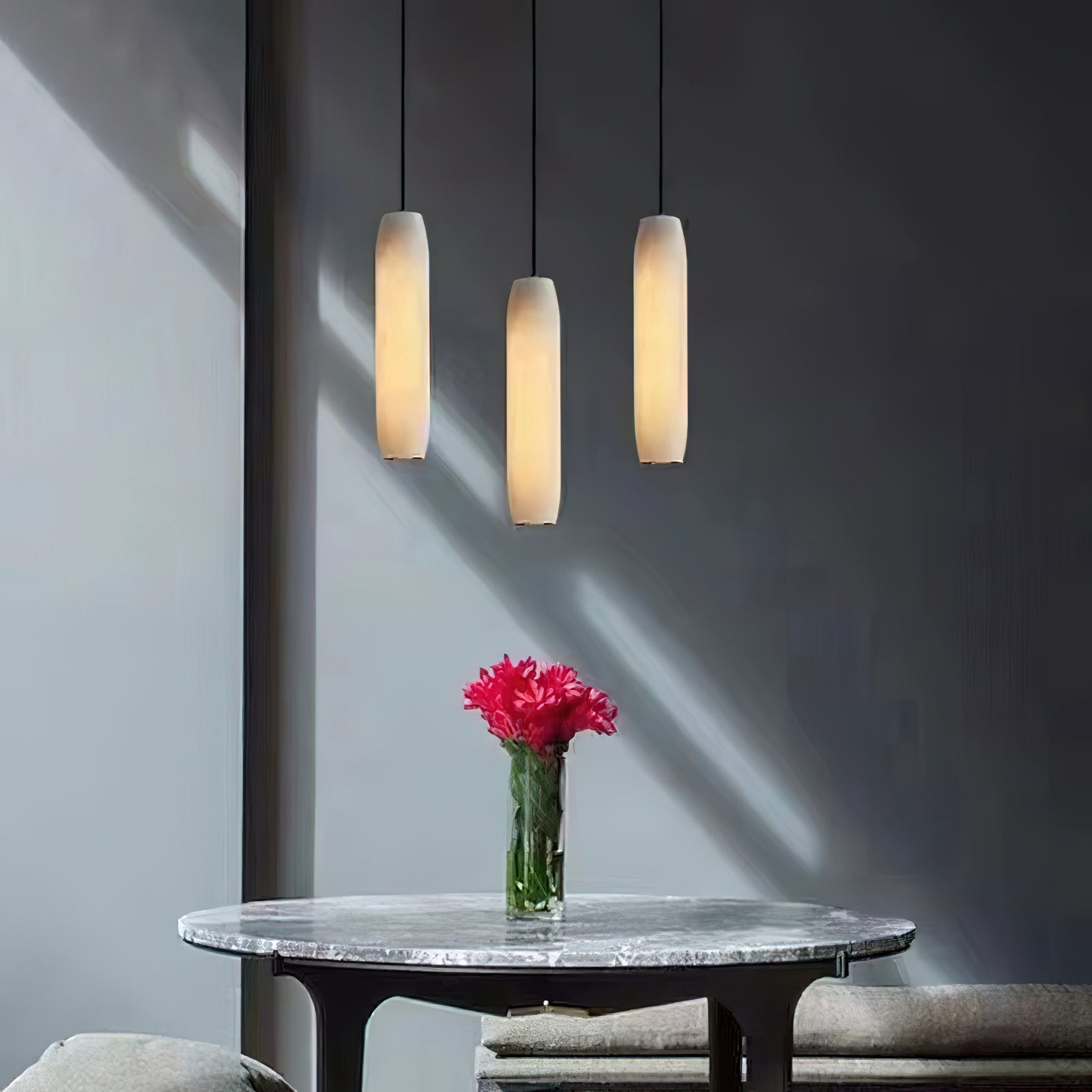 Clérachic groups three Asbury pendants at staggered drops on a sunlit grey wall, over a marble table with carnations.