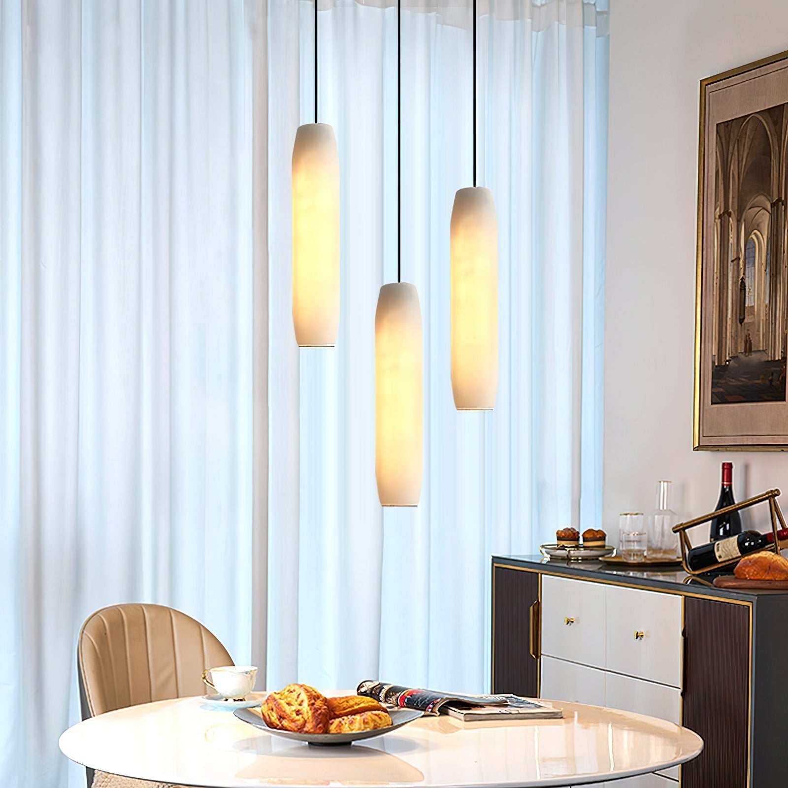 The Clérachic Asbury trio hangs close to a sheer-curtained window, above a round table and a brass-trimmed sideboard.