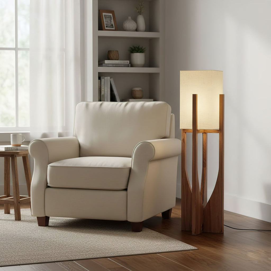 A Clérachic floor lamp with a lit fabric shade stands beside a cream armchair and a bookshelf in a bright living room.