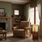 Lit Clérachic wood-framed lamp beside a tan wooden armchair, in a room with a stone fireplace and sage-green walls.