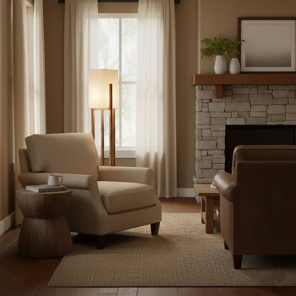 Slim wooden floor lamp from Clérachic glowing by a window with cream curtains, above a woven rug and a beige armchair.