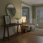 Floor lamp from Clérachic beside a dark console table with a round mirror, a framed print and a small plant above.