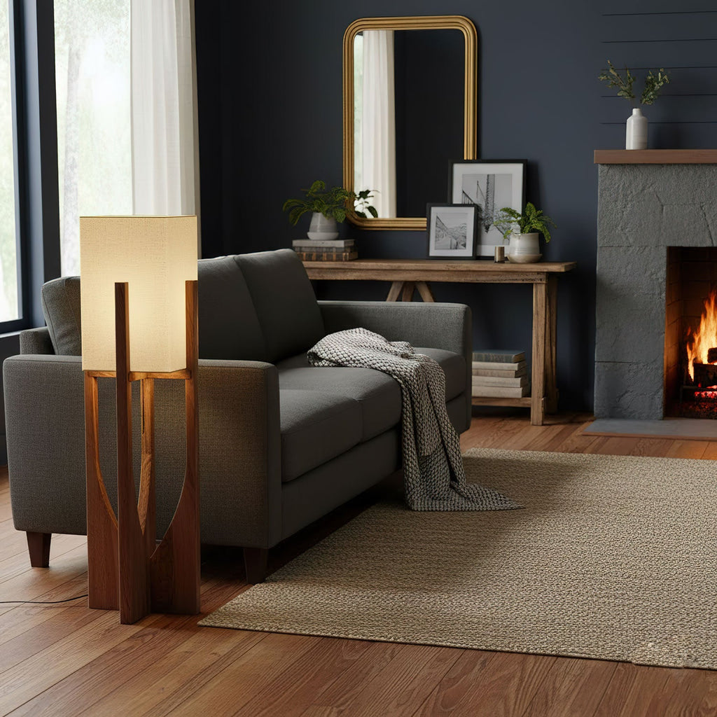 Wood-framed Clérachic floor lamp beside a grey sofa and a fireplace with a lit fire, in a room with deep navy walls.