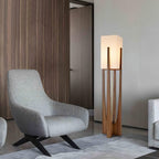Tall wooden floor lamp from Clérachic beside a grey lounge chair, in front of a wall of dark wood panelling.