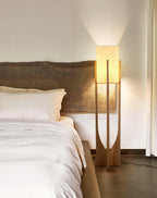 Floor lamp from Clérachic, its fabric shade lit, standing at a bedside by a live-edge wooden headboard and white bedding.