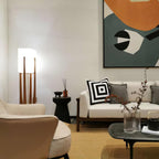 Slim Clérachic floor lamp in the corner of a bright living room, near a cream sofa, a black side table and a bold abstract painting.