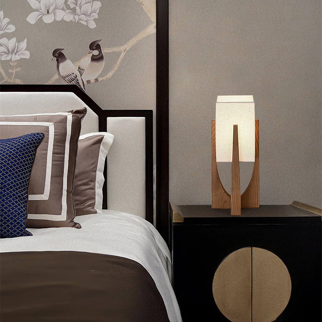 Small Clérachic wood lamp with a white fabric shade on a black lacquered cabinet beside a bed with cushions in navy and brown.