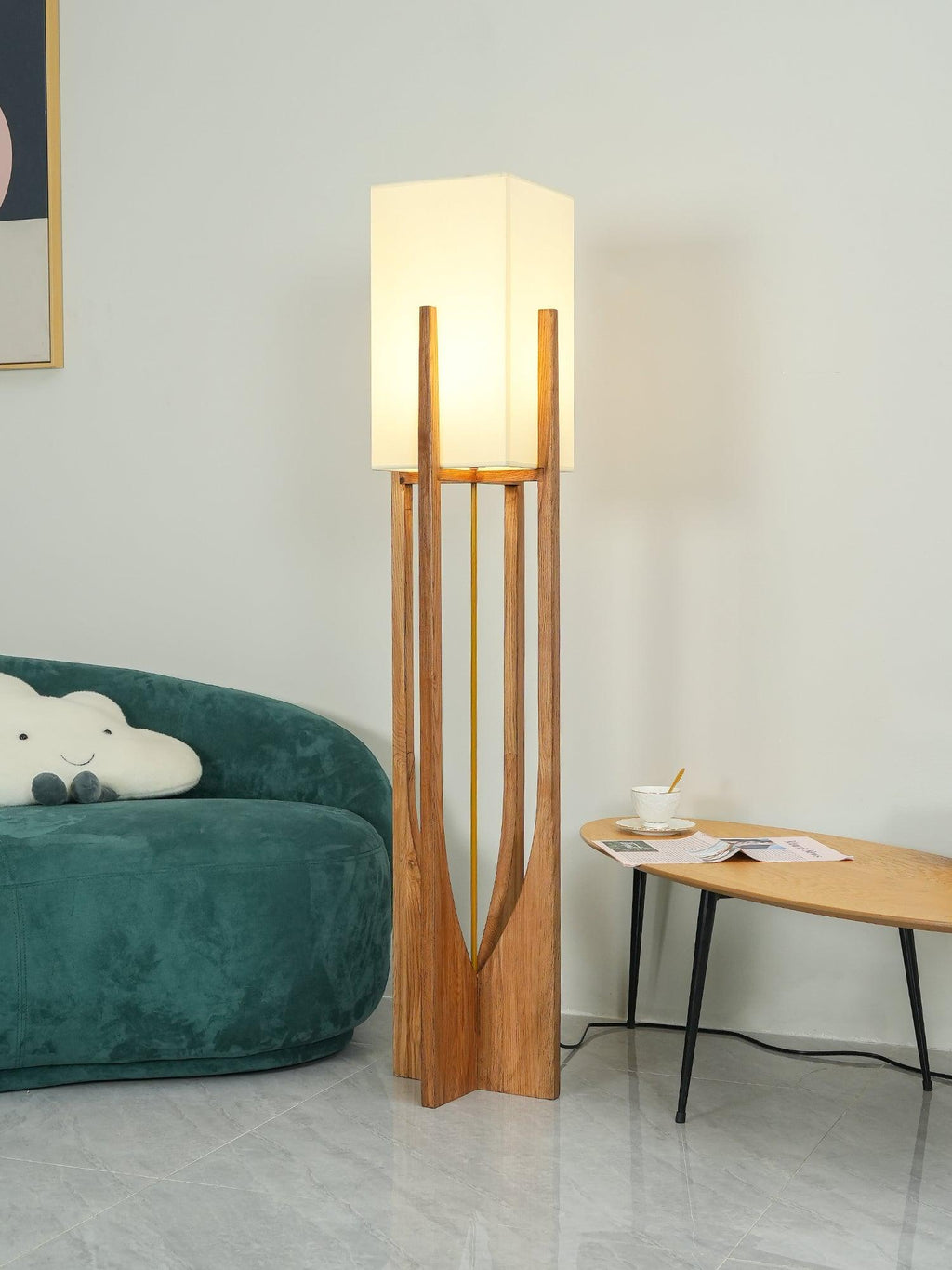 Natural wood floor lamp from Clérachic with its shade lit, beside a green velvet sofa and a small oval wooden table.