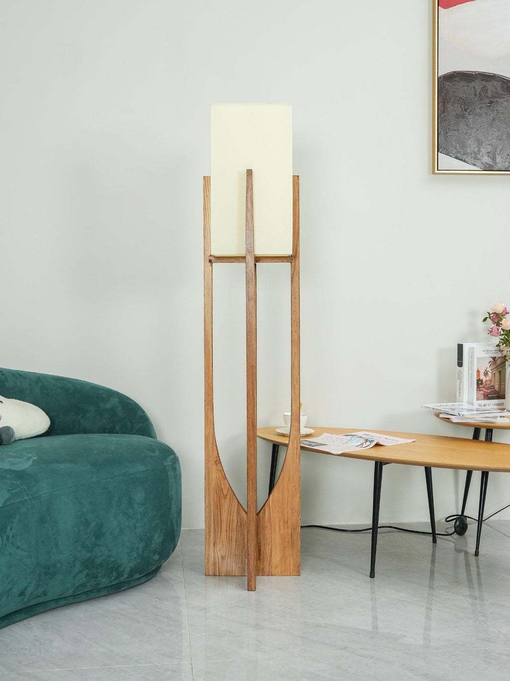 Clérachic natural wood floor lamp, unlit, with a white fabric shade, beside a green velvet sofa and a framed print.