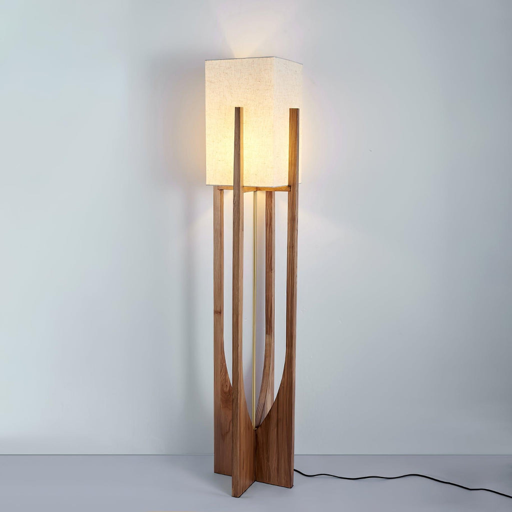 Lit Clérachic floor lamp in a dark wood frame, with a warm glow on the wall above and a black cord trailing on the floor.