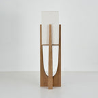 Close view of the base and lower half of this Clérachic floor lamp in natural wood, with its curved cut-out and cross-shaped foot.