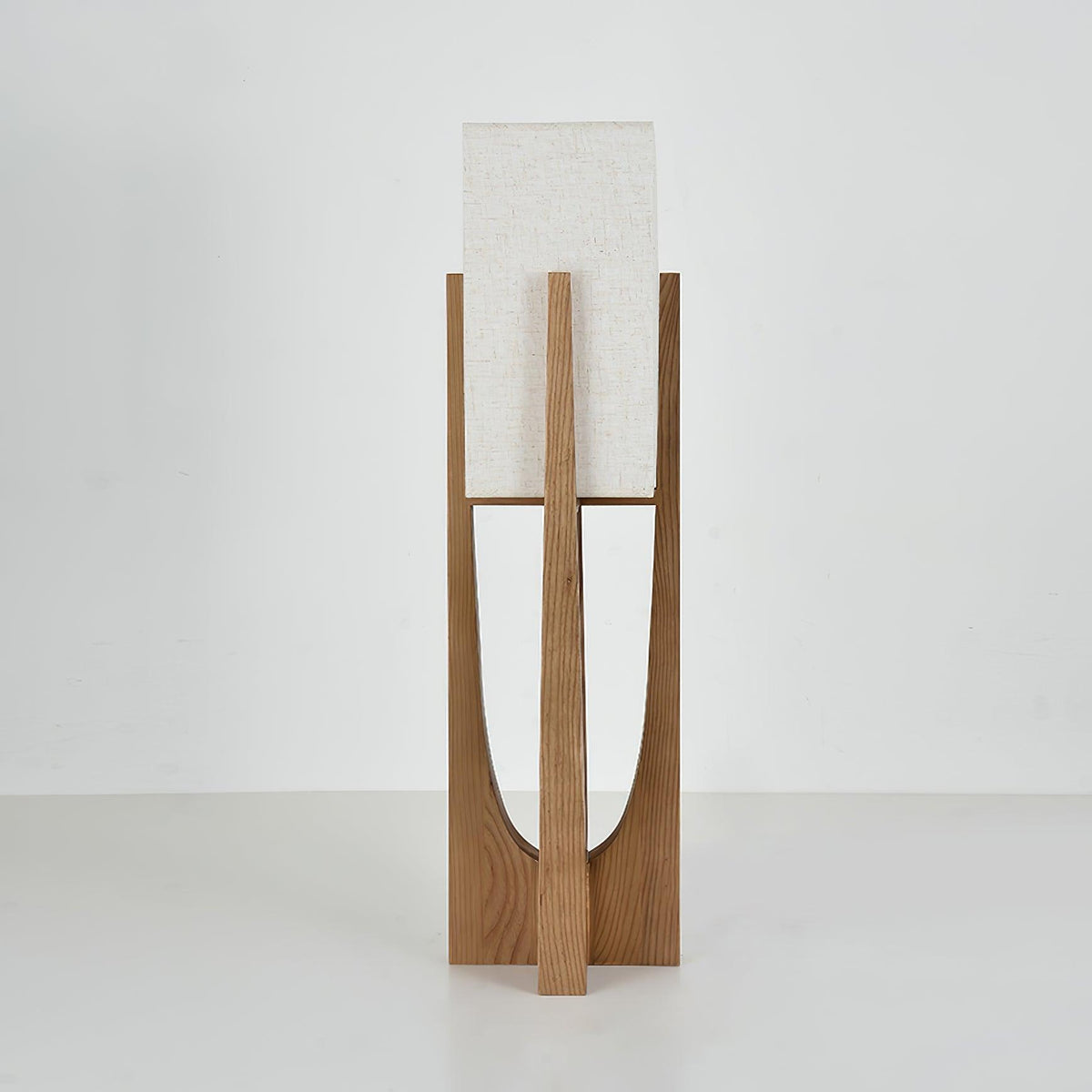 Close view of the base and lower half of this Clérachic floor lamp in natural wood, with its curved cut-out and cross-shaped foot.