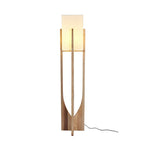Tall Clérachic floor lamp in natural ash with a softly lit shade and a black cord on the floor, on a white backdrop.