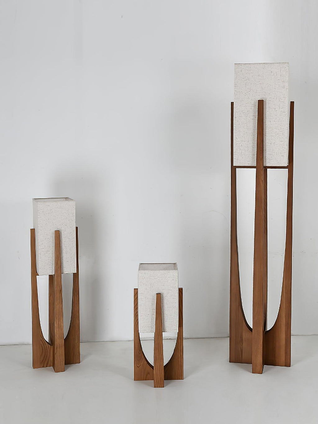 Three Clérachic lamps in different heights stand together against a pale wall, all with unlit white fabric shades.