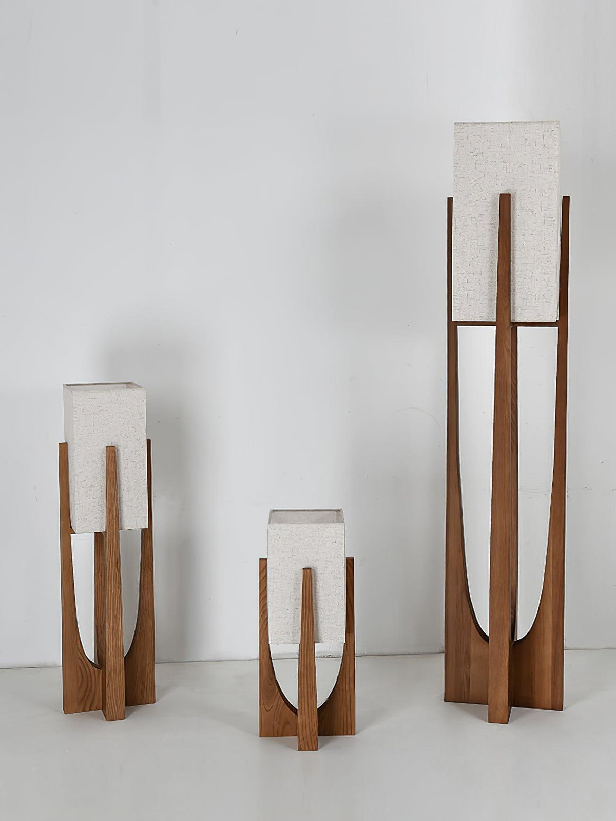 Three Clérachic lamps in different heights stand together against a pale wall, all with unlit white fabric shades.