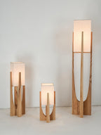 Three Clérachic lamps lit together, with warm light in the shades of the two shorter ones, against a pale wall.