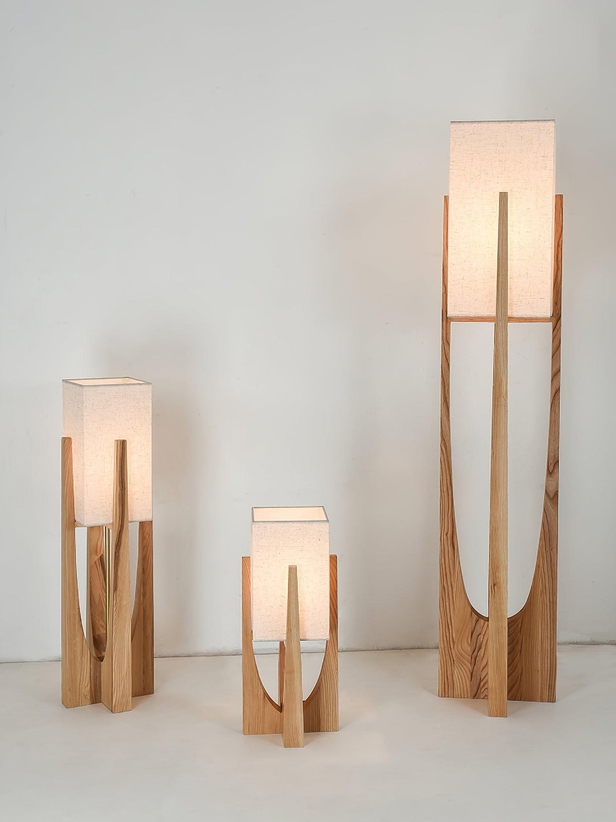 Three Clérachic lamps lit together, with warm light in the shades of the two shorter ones, against a pale wall.