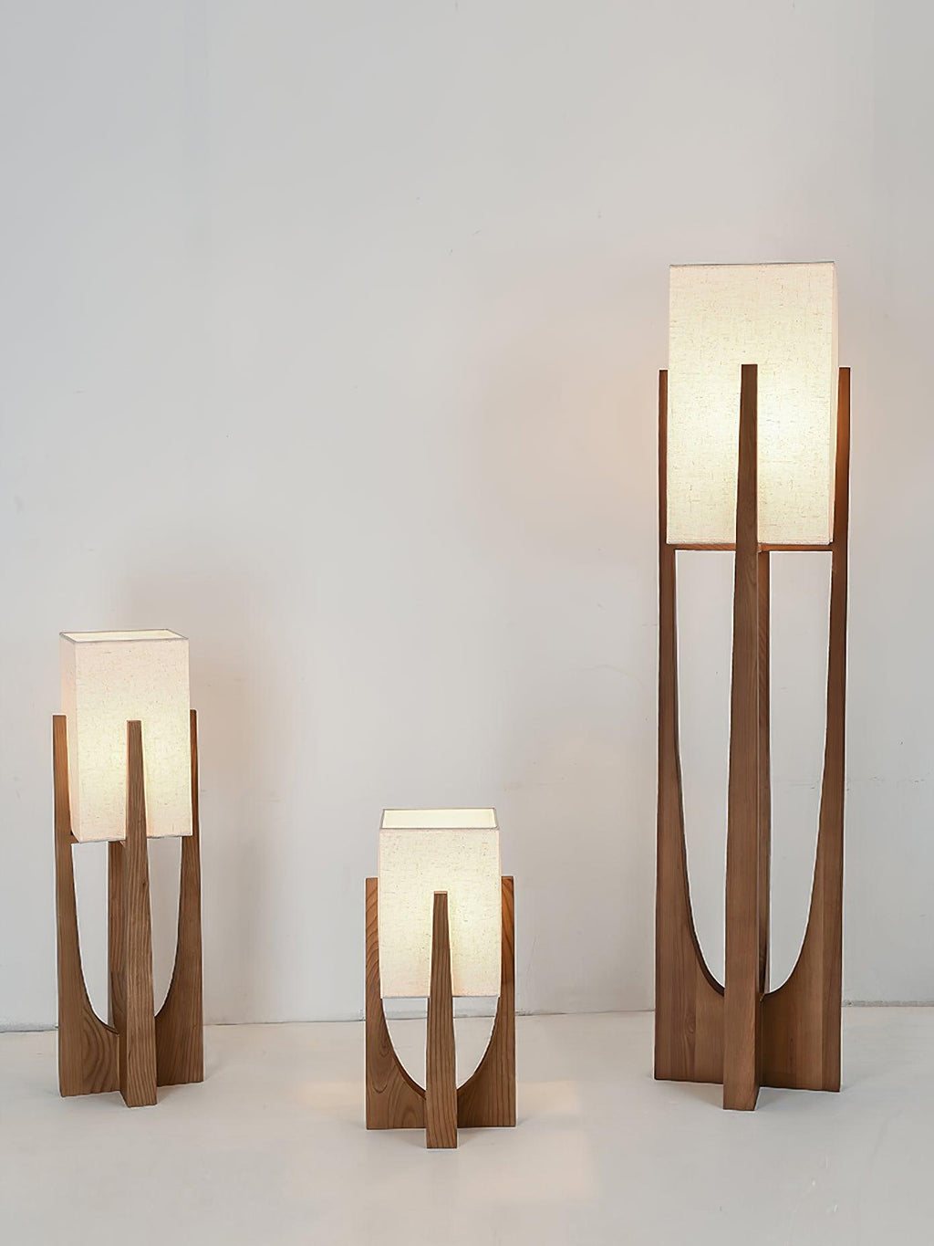 Three Clérachic lamps in dark wood stand side by side, the two shorter ones lit and the tallest unlit, on a pale floor.