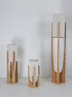Three Clérachic lamps in natural wood stand together against a pale wall, with their shades unlit.