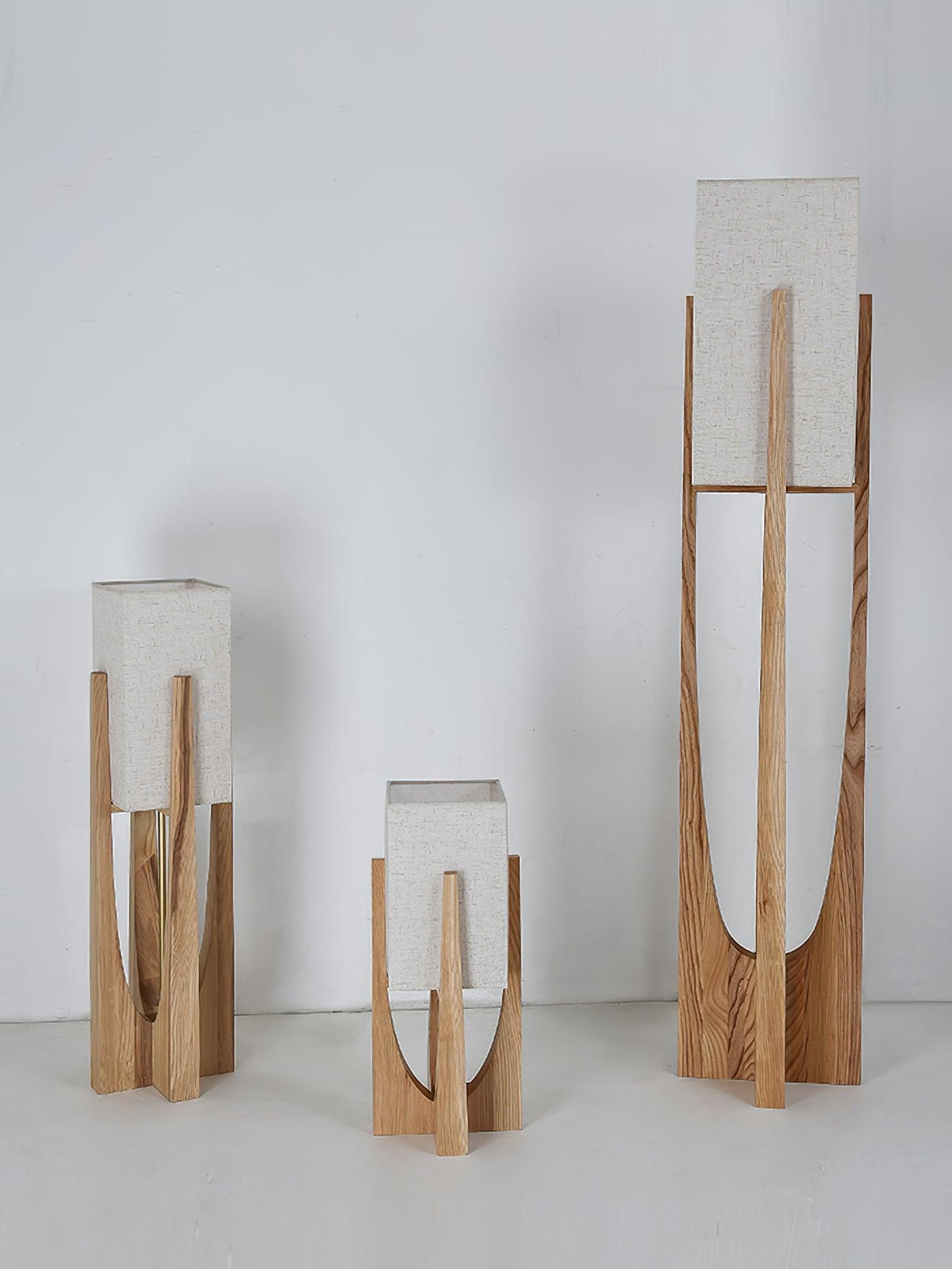Three Clérachic lamps in natural wood stand together against a pale wall, with their shades unlit.