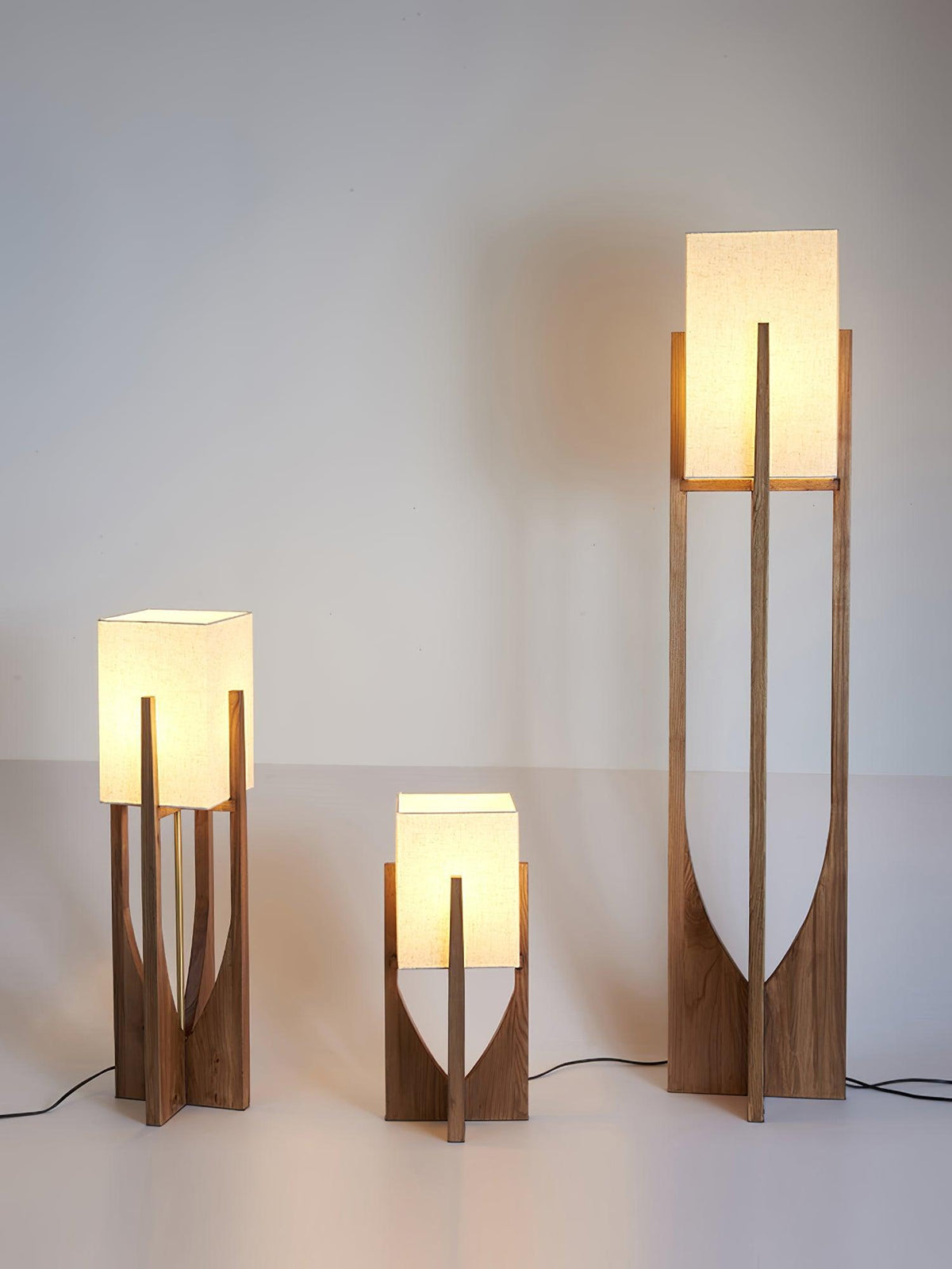 Three Clérachic lamps in different heights, all lit and glowing, against a pale grey wall with a warm shadow behind them.