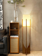 Tall Clérachic floor lamp glowing beside a narrow cane-front cabinet with a glass vase of branches, near a black leather sofa.