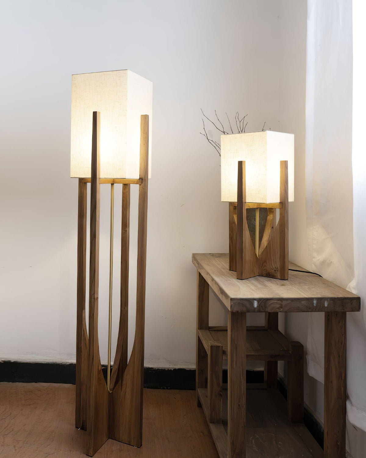 Tall and short Clérachic lamps in dark wood side by side, the tall one lit, with a rustic wooden table beside them.
