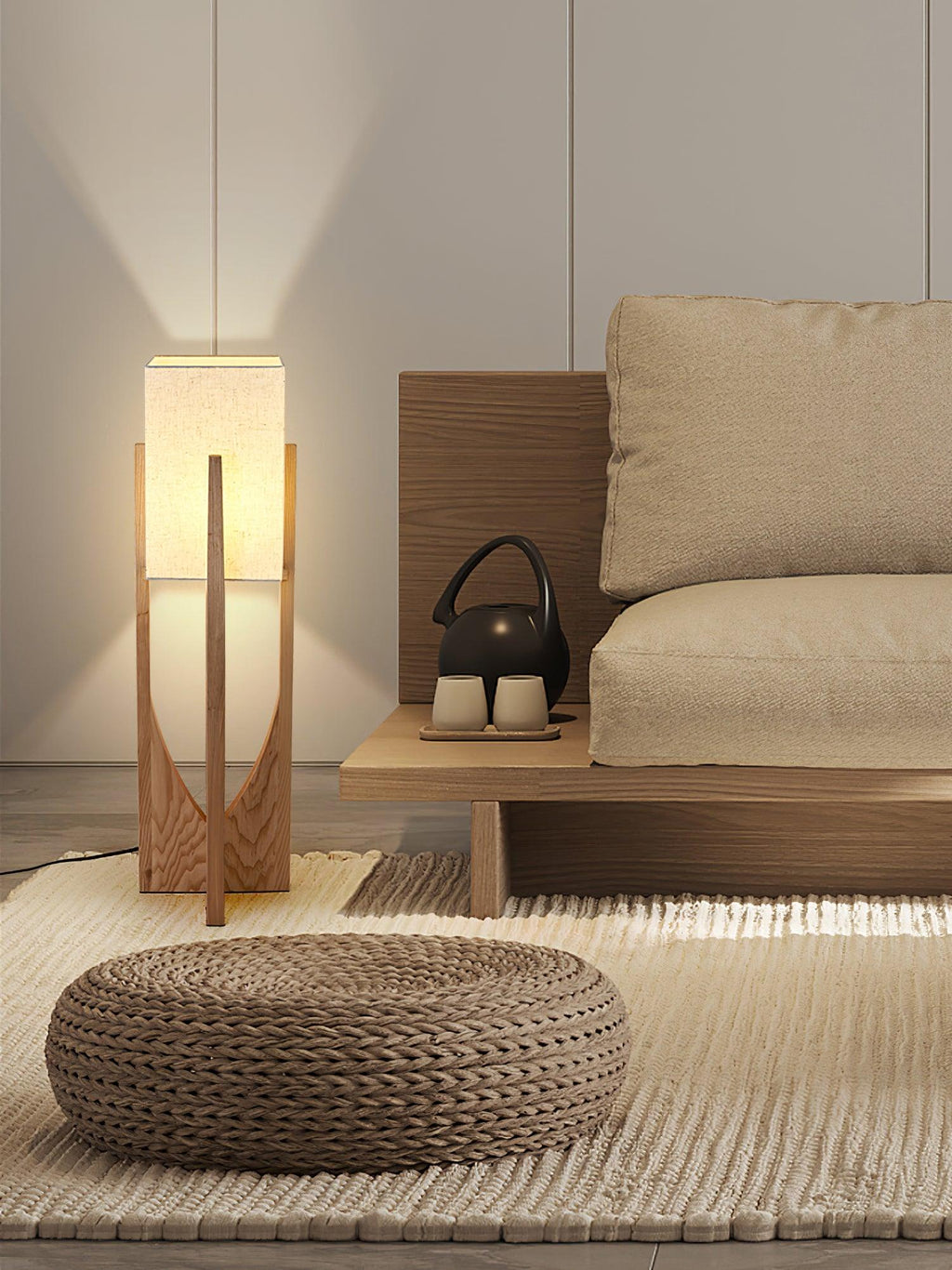 Clérachic floor lamp, lit, on a woven rug beside a low sofa and a round pouf, with a teapot on a low wooden bench.