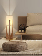 Clérachic floor lamp, lit, on a woven rug beside a low sofa and a round pouf, with a teapot on a low wooden bench.