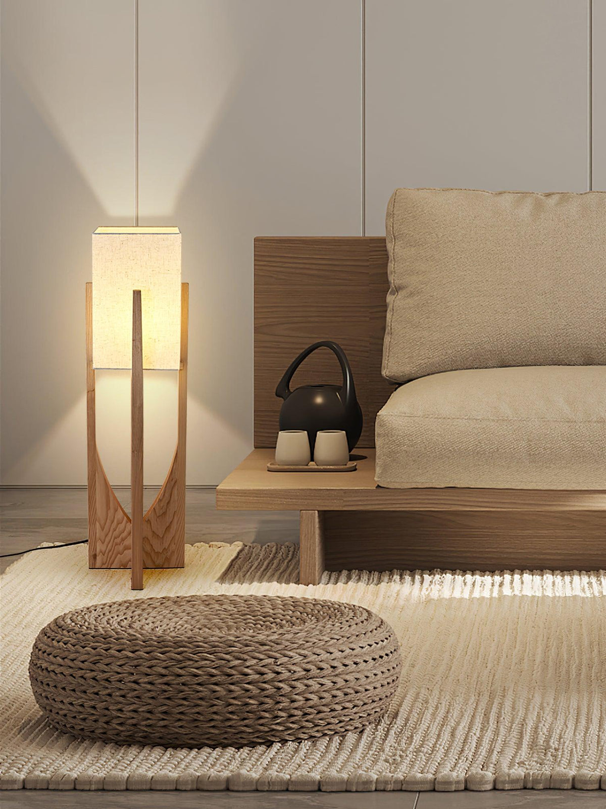 Clérachic floor lamp, lit, on a woven rug beside a low sofa and a round pouf, with a teapot on a low wooden bench.