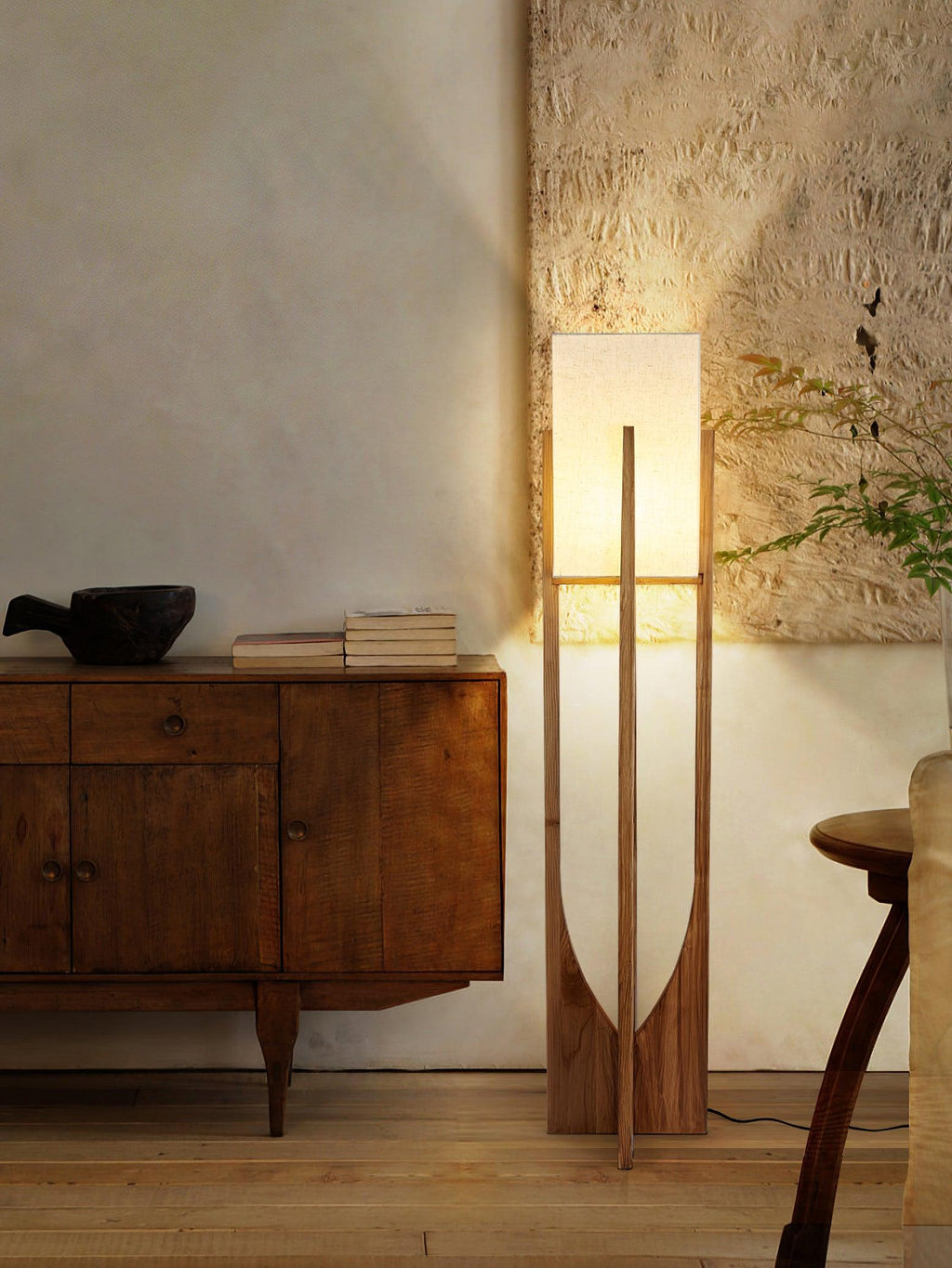 Lit Clérachic floor lamp beside a wooden cabinet with a dark bowl, with a rough plaster wall glowing above it.