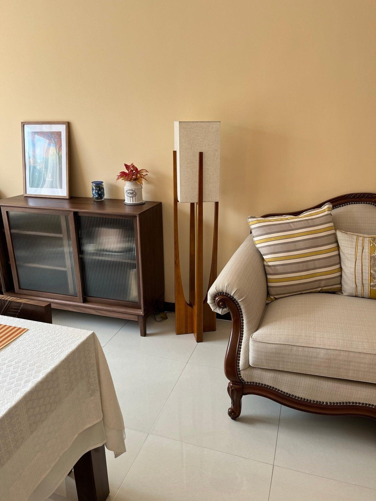 Clérachic floor lamp against a warm yellow wall, beside a dark cabinet and a cream sofa with striped cushions.
