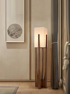 Clérachic floor lamp lit beside a window with grey curtains, in front of a framed round artwork on a cream wall.
